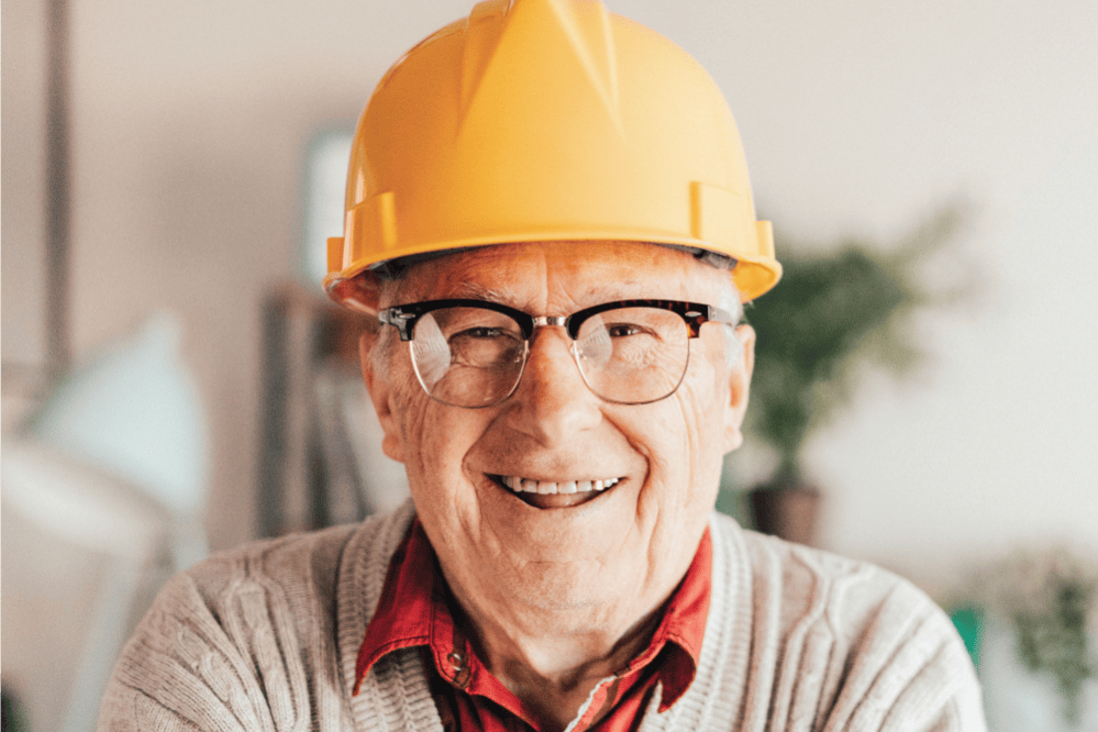 Senior man smiling with a yellow hard hat on